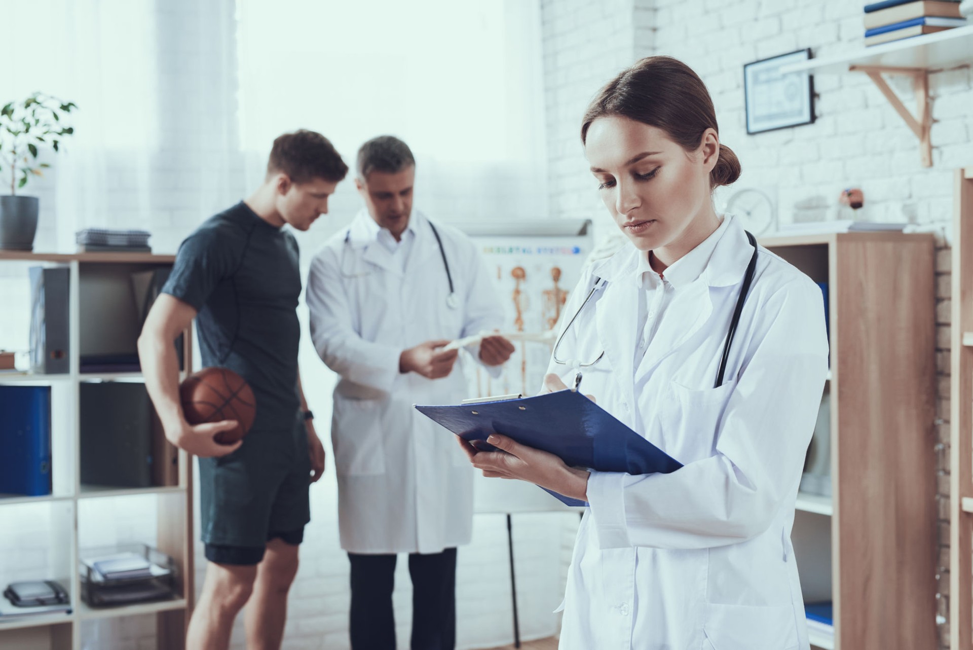 Male and female doctors with stethoscopes in office. Doctor is talking to basketball player.